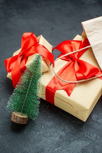 Vista frontal de lindos presentes com fita vermelha e árvore de Natal em uma mesa escura