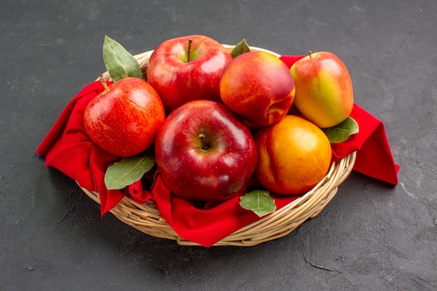 Vista frontal de maçãs frescas com pêssegos dentro de uma cesta na mesa escura com frutas frescas maduras