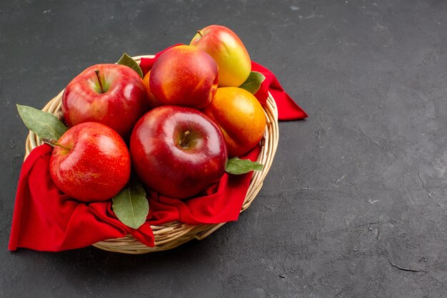 Vista frontal de maçãs frescas dentro de uma cesta em uma mesa escura.