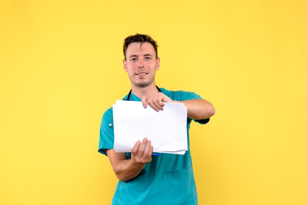 Vista frontal de médico segurando documentos na parede amarela