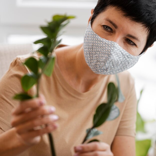 Vista frontal de mulher com máscara facial cuidando de plantas de interior