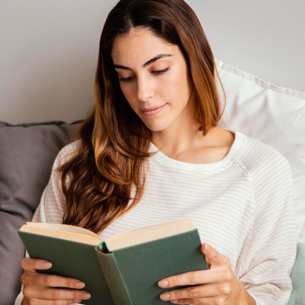 Vista frontal de mulher lendo um livro em casa