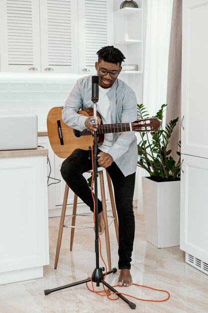 Vista frontal de músico masculino em casa tocando violão com microfone