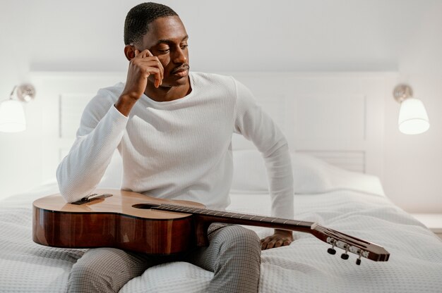 Vista frontal de músico masculino na cama com violão