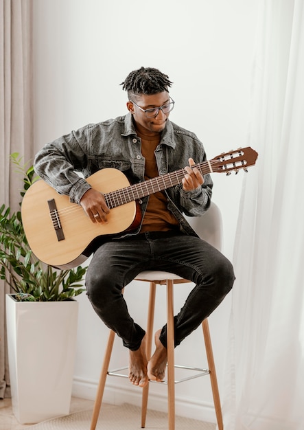 Vista frontal de músico tocando violão em casa