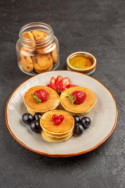 Vista frontal de panquecas deliciosas com frutas em uma superfície escura, torta de frutas e bolo doce