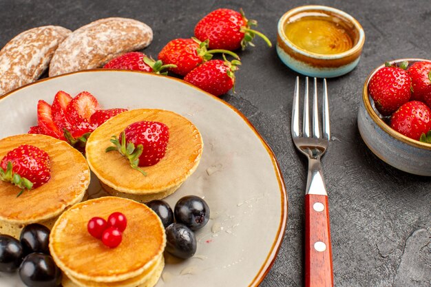 Vista frontal de panquecas deliciosas com frutas em uma superfície escura, torta de frutas e bolo doce