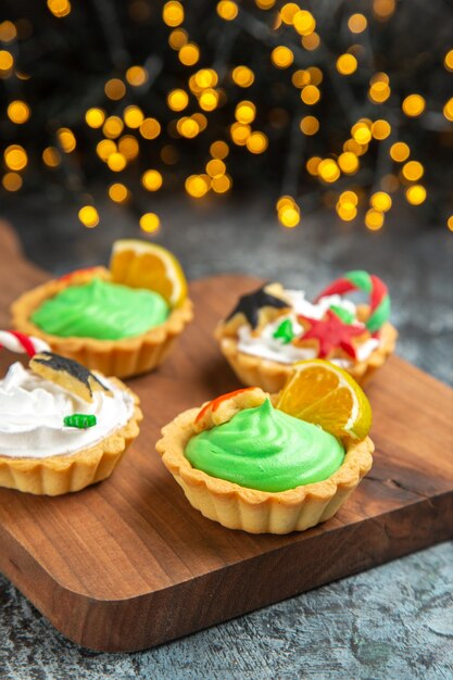 Vista frontal de pequenas tortas em uma tábua em uma superfície escura isolada com luzes de natal