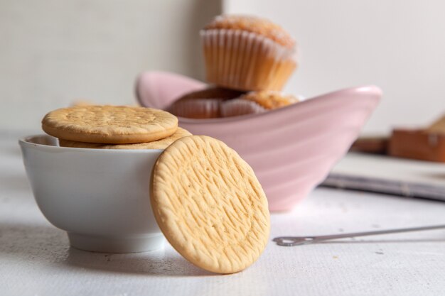 Vista frontal de pequenos bolos deliciosos com açúcar em pó e biscoitos na superfície branca