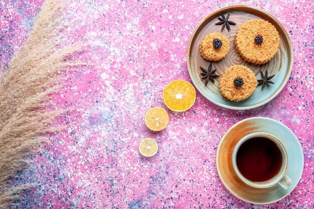 Vista frontal de pequenos bolos gostosos, doce e delicioso prato interno com chá na superfície rosa