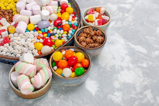 Vista frontal de perto, composição de doces de diferentes cores e marshmallow na mesa branca