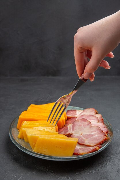 Vista frontal de perto da mão segurando o garfo em um prato azul com deliciosos petiscos em um fundo preto