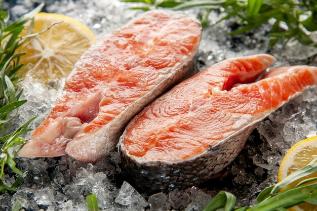Vista frontal de perto fatias de peixe fresco com limão e gelo na foto cor escura prato carne comida escuridão frutos do mar