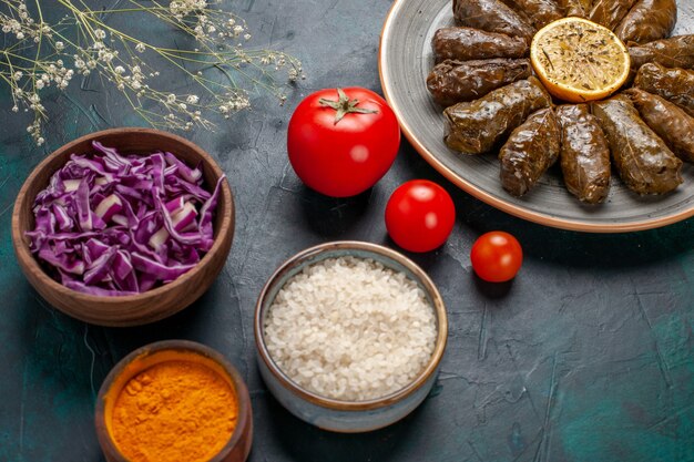 Vista frontal de perto folha dolma deliciosa refeição de carne oriental enrolada dentro de folhas verdes com tomates e temperos na mesa azul