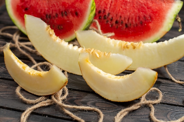 Foto grátis vista frontal de perto melancia cortada em fatias de fruta doce com melão no fundo marrom rústico