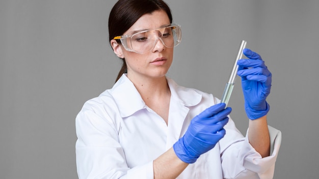 Vista frontal de pesquisadora com óculos de segurança segurando um tubo de ensaio