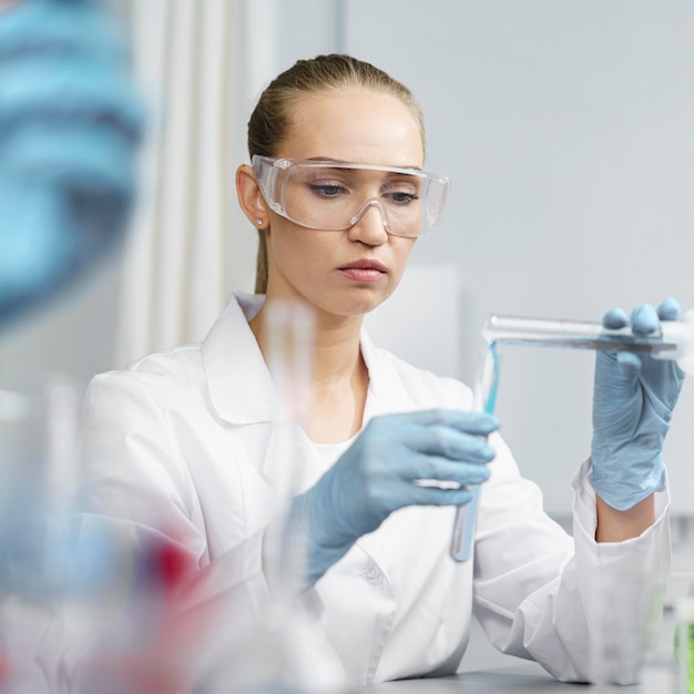 Vista frontal de pesquisadora no laboratório com tubos de ensaio e óculos de segurança