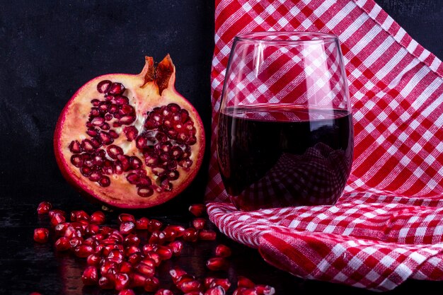 Vista frontal de romã picada com suco de romã em um copo com uma toalha vermelha