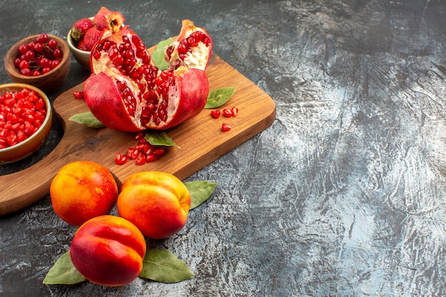 Vista frontal de romãs fatiadas com pêssegos na mesa escura das frutas da árvore do jardim