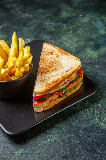 Vista frontal de sanduíches de presunto com batatas fritas dentro do prato em superfície escura