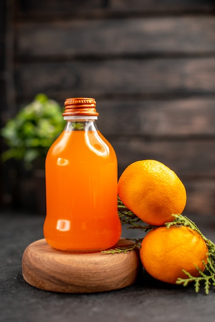 Vista frontal de suco de laranja em garrafa na placa de madeira laranjas na superfície isolada marrom