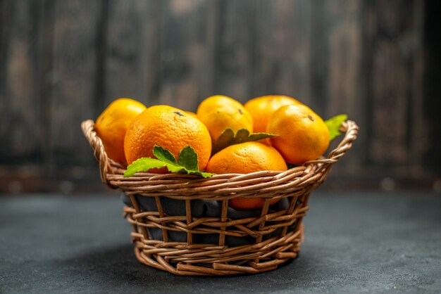 Vista frontal de tangerinas frescas em cesta de vime em local escuro