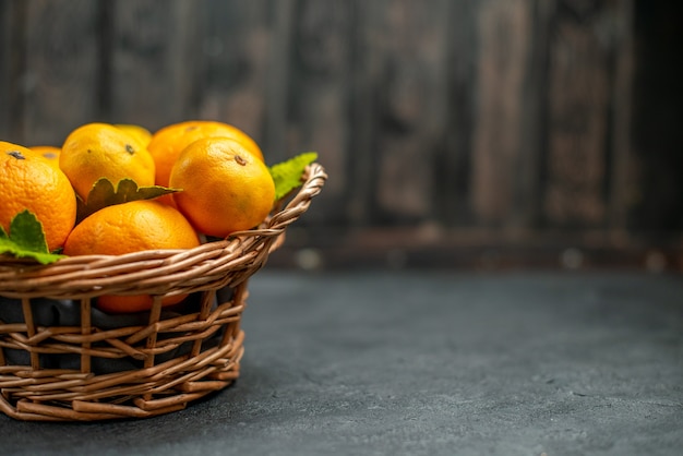 Vista frontal de tangerinas frescas em cesta de vime em local escuro