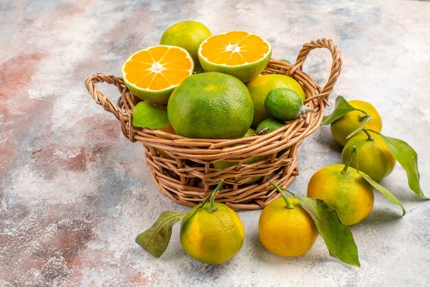 Vista frontal de tangerinas frescas em uma cesta de vime cercadas por tangerinas em um fundo nu