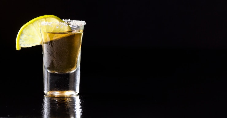 Foto grátis vista frontal de tequila dourada com limão e cópia-espaço