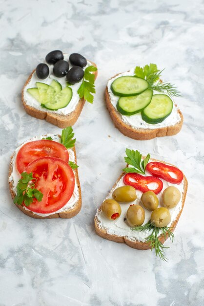 Vista frontal de torradas saborosas com tomates, azeitonas, pimentões e pepinos em branco