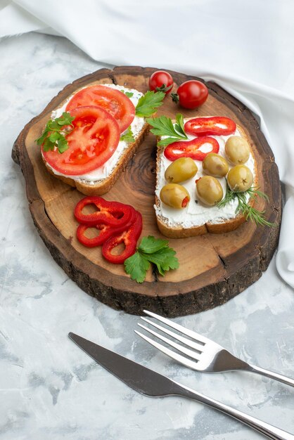 Vista frontal de torradas saborosas com tomates e azeitonas em uma tábua de madeira branca