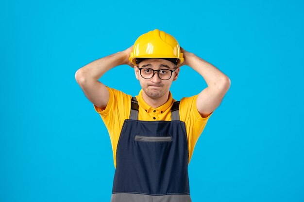 Vista frontal de trabalhador masculino estressado de uniforme e capacete em um trabalhador braçal de piso azul