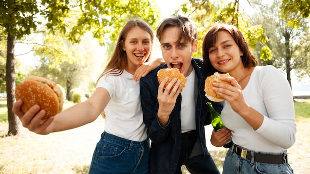 Vista frontal de três amigos no parque com cerveja e hambúrgueres