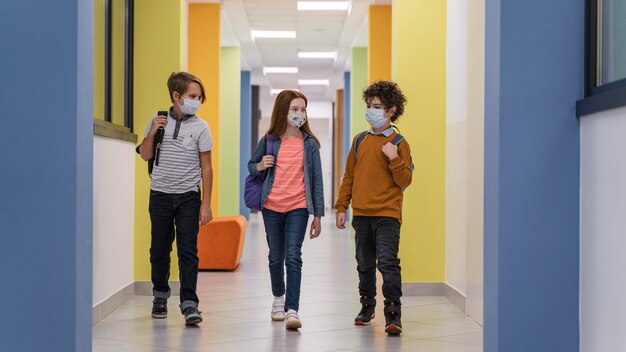 Vista frontal de três crianças no corredor da escola com máscaras médicas