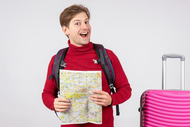 Vista frontal de turista masculino com mochila e mapa na parede branca