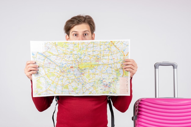 Vista frontal de turista masculino com mochila e mapa na parede branca