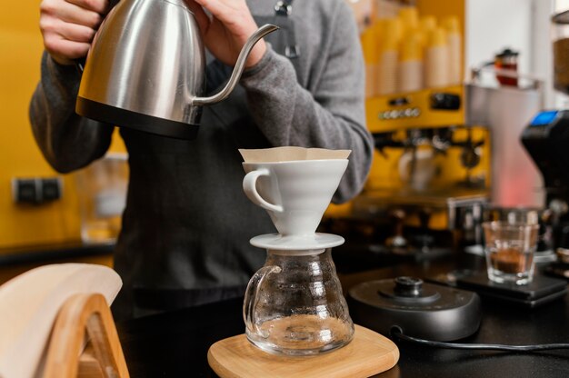 Vista frontal de um barista despejando água fervente em um filtro de café