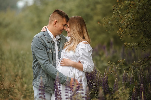 Vista frontal de um casal caucasiano recém-casado esperando um bebê, quase se beijando em um prado com flores de tremoço