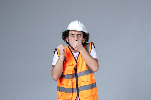 Vista frontal de um construtor masculino a pensar usando colete de advertência com capacete de segurança na parede de onda cinza