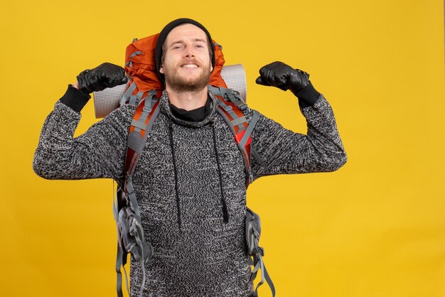 Vista frontal de um homem confiante caroneiro com luvas de couro e mochila vermelha mostrando os músculos do braço