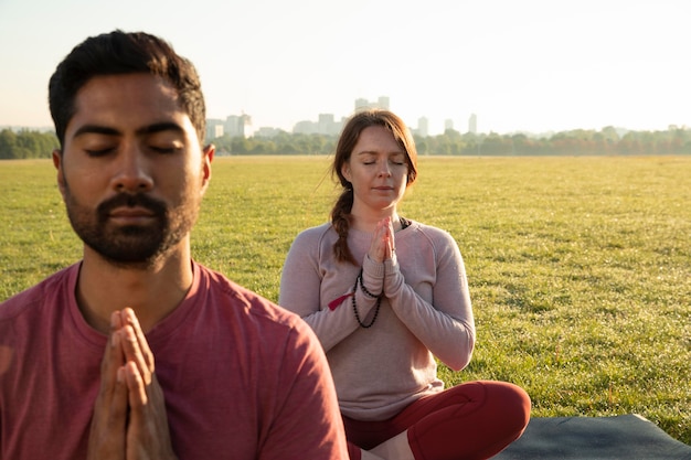 Vista frontal de um homem e uma mulher meditando ao ar livre em esteiras de ioga