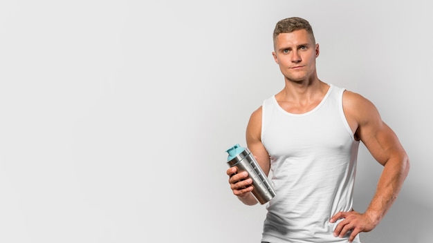 Vista frontal de um homem em forma posando com uma camiseta regata e segurando uma garrafa de água