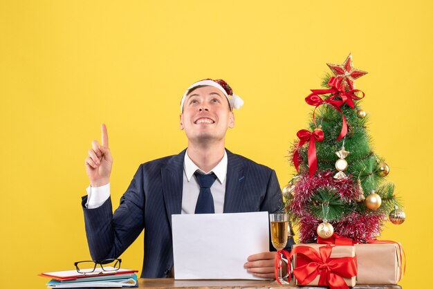 Vista frontal de um homem exultante olhando para uma mesa alta perto da árvore de natal e presentes em amarelo