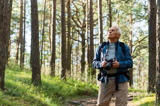 Vista frontal de um homem idoso com uma mochila explorando a natureza