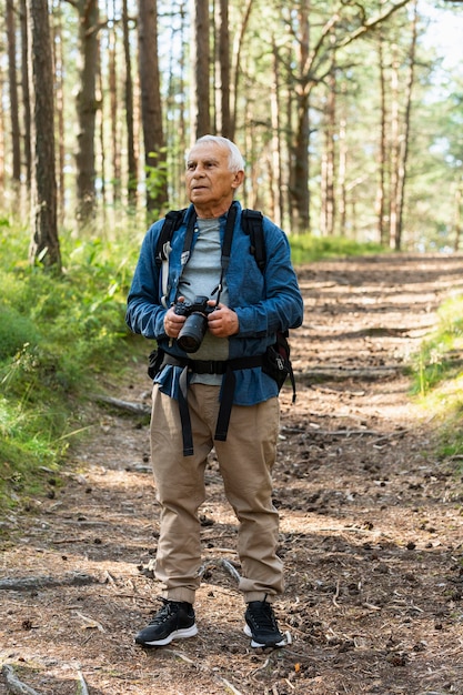 Vista frontal de um homem mais velho viajando com mochila e câmera na natureza