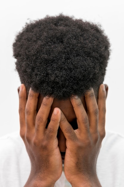 Vista frontal de um homem negro chorando com as mãos cobrindo o rosto