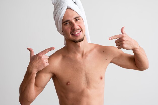 Vista frontal de um homem sem camisa com uma toalha na cabeça apontando para si mesmo