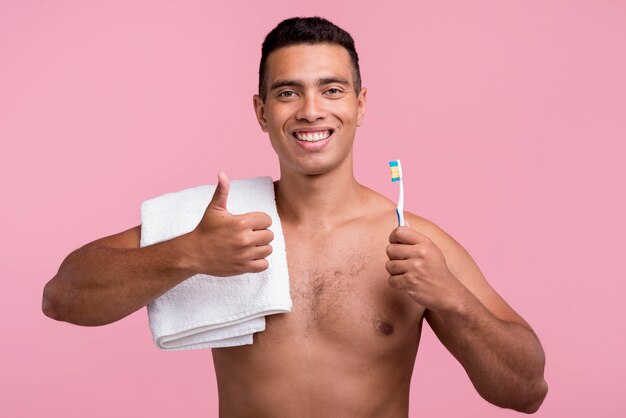 Vista frontal de um homem sem camisa segurando a escova de dentes e levantando os polegares