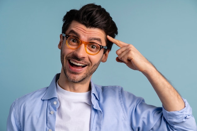 Vista frontal de um homem sorridente com óculos apontando para a cabeça