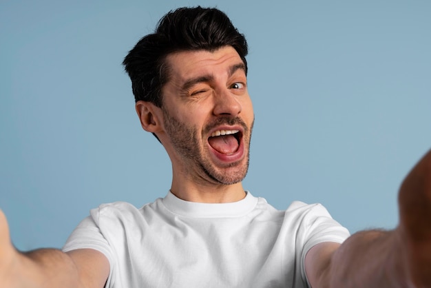 Vista frontal de um homem sorridente tirando uma selfie e piscando o olho